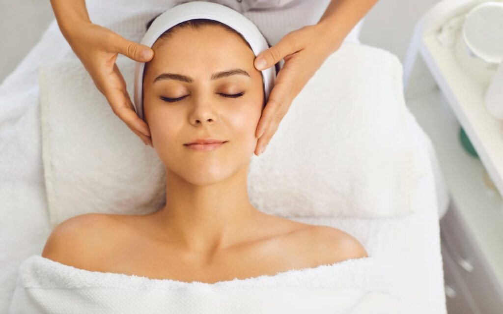 Woman receiving a relaxing facial massage at a spa on a cruise ship, eyes closed and wrapped in a white towel.