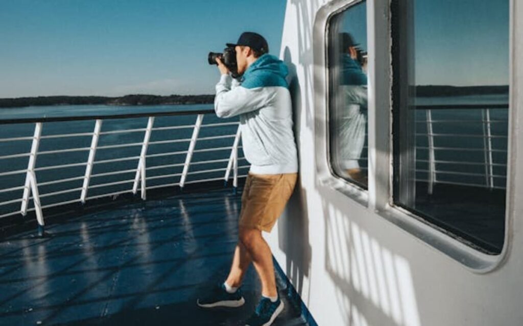 Man taking a photo on a cruise ship deck with ocean and railing in the background.