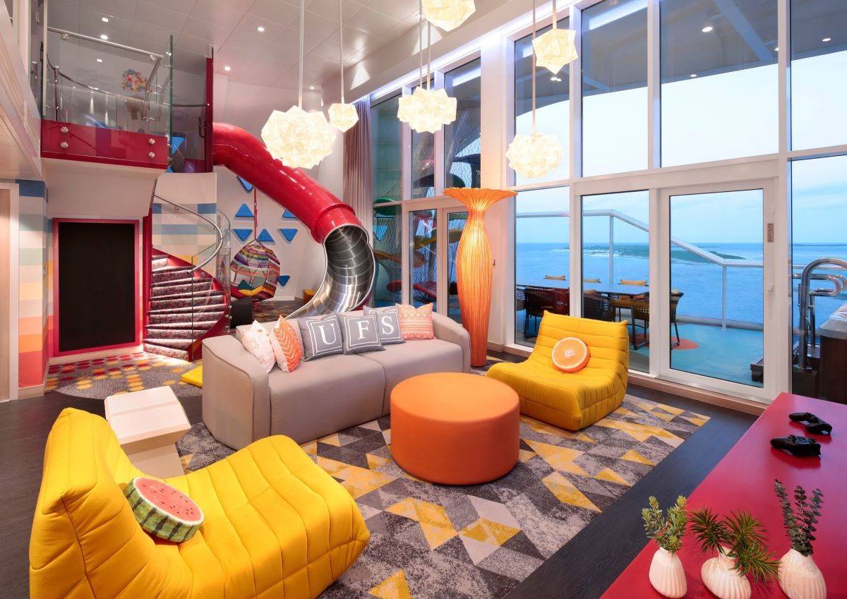 The Ultimate Family Suite on Wonder of the Seas, showcasing a playful and colorful interior with a large red slide, vibrant furniture, and ocean views. This family-friendly space includes a swing, a floor-to-ceiling window, and creative elements designed for fun and relaxation.