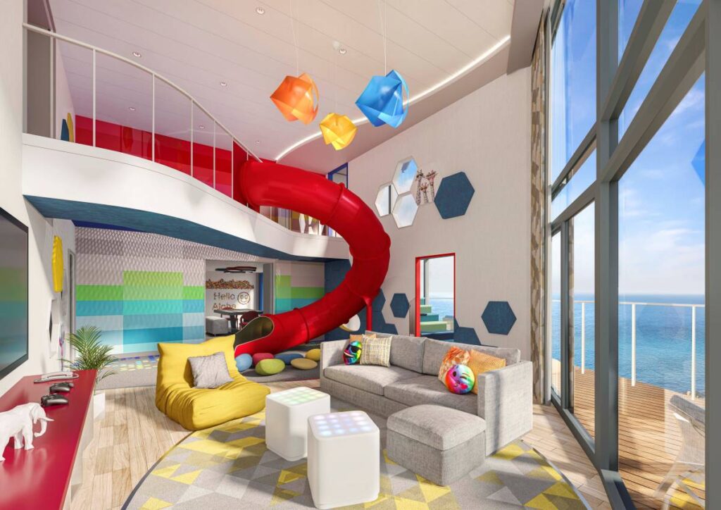 Interior of the Ultimate Family Townhouse on Royal Caribbean's Icon of the Seas, featuring a bold red slide, multicolored hanging lights, and a cozy living area with a plush yellow chair and gray sectional sofa. The room is bathed in natural light from floor-to-ceiling windows that offer a panoramic view of the sea.
