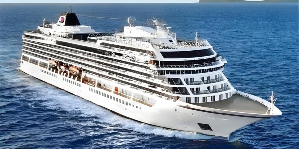 Aerial view of a Viking Ocean cruise ship sailing through deep blue water, showing its clean-lined white exterior, tiered balconies, and forward-facing observation decks under clear skies.