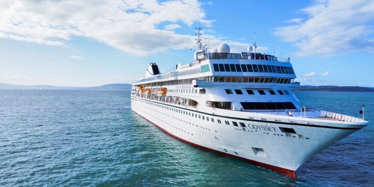 The Villa Vie Odyssey cruise ship sails through calm blue waters under a bright sky, showcasing its white exterior, panoramic windows, and spacious decks. The mid-sized vessel is designed for long-term living and global exploration, reflecting the unique lifestyle of the Villa Vie Odyssey cruise ship.