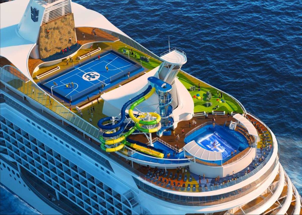 Royal Caribbean's Voyager of the Seas offers a vibrant top-deck experience with a colorful water slide, sports court, and rock-climbing wall, captured with the deep blue ocean stretching into the distance.