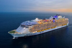 The majestic Royal Caribbean's Wonder of the Seas cruises at sunset, with its innovative structure highlighted by the fading sunlight. The world's largest cruise ship is a marvel of modern engineering, boasting a unique combination of luxurious amenities and cutting-edge design as it traverses the open ocean.