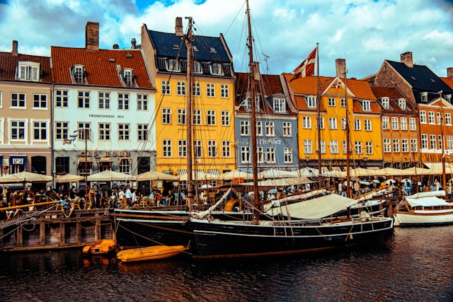 Colorful historic buildings lining Copenhagen, Denmark's waterfront harbor with sailboats docked along the quay in a European port city.