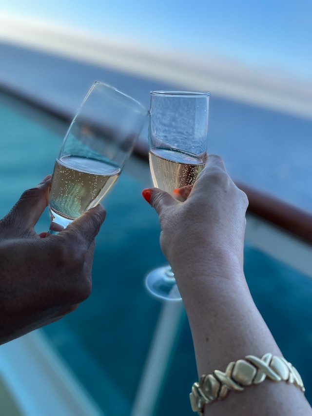 Couple clinking champagne flutes on a ship's balcony with blue ocean in background
