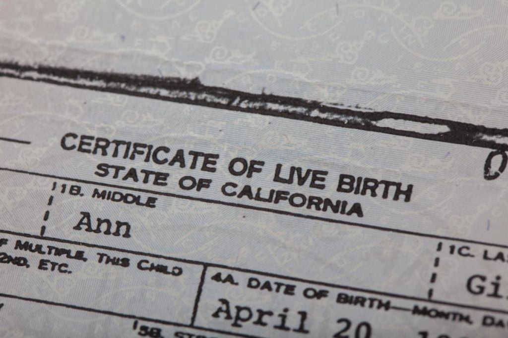 Close-up view of a California Certificate of Live Birth document, with visible text headers and partial obscured personal details