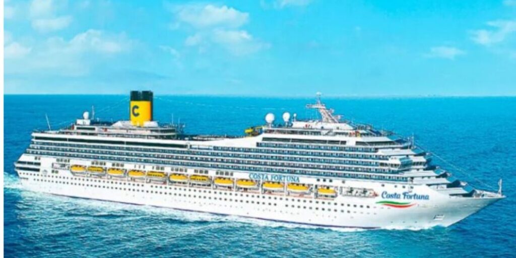 The Costa Fortuna cruise ship sails on a calm blue sea, with its distinctive yellow lifeboats lined up along the white decks and the large yellow funnel bearing the Costa logo. The clear skies and serene ocean set a peaceful scene for a voyage.
