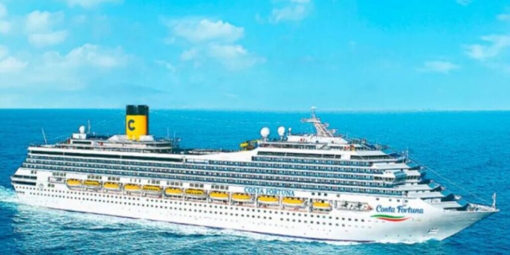 The Costa Fortuna is an impressive vessel, showcased here against the stunning backdrop of an expansive blue ocean and a clear sky that stretches on the horizon. The ship's white superstructure with generous rows of balconies promises an inviting and luxurious experience. Prominently displayed on the funnel is the Costa Cruises logo, a yellow "C" against a navy background, which stands out as a symbol of the line’s rich Italian heritage and style. The deck is dotted with satellite dishes and other navigational equipment, signifying modern amenities and connectivity even at sea. The Costa Fortuna, with its grand scale and elegant design, seems ready to offer its passengers a memorable voyage.