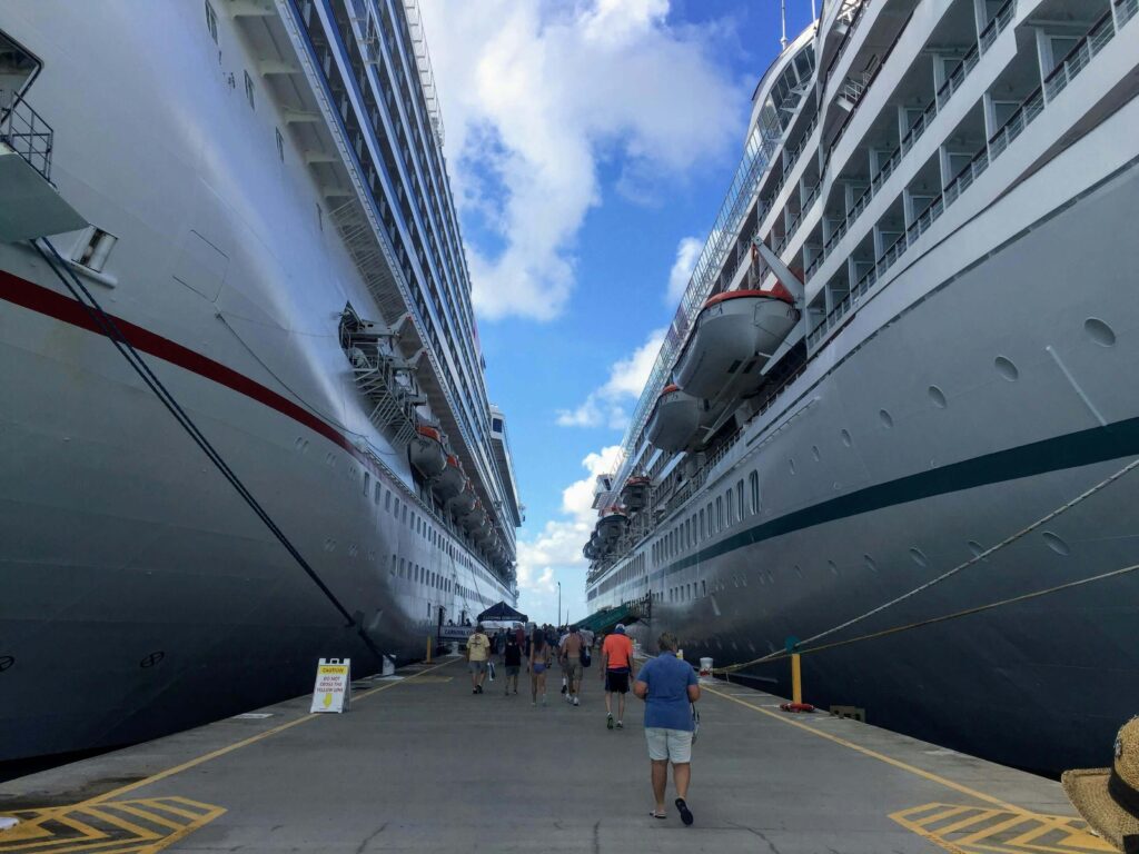 Cruise passengers walking along a pier near a cruise port terminal between large cruise ships.