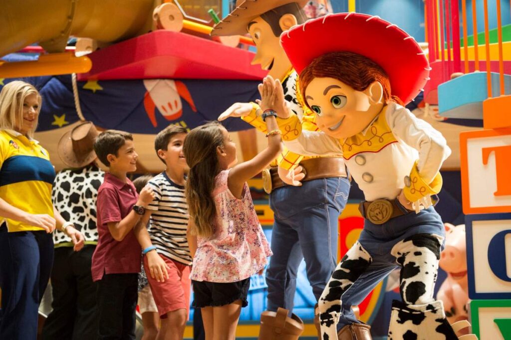 Children engaging with life-sized figures of Woody and Jessie in Andy's Room play area on the Disney Wonder, surrounded by colorful oversized toy blocks and a playful decor inspired by the Toy Story movies.