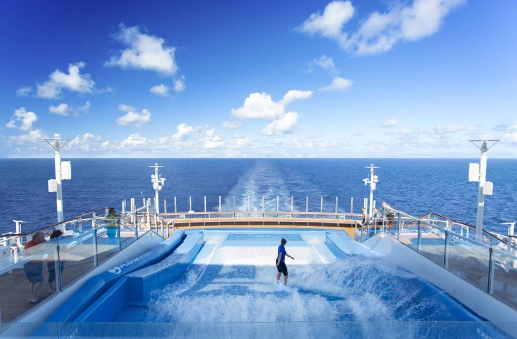 A person enjoys surfing on the Flowrider simulator aboard Royal Caribbean's Anthem of the Seas, with the endless ocean and a clear blue sky in the background, capturing the essence of adventure at sea.
