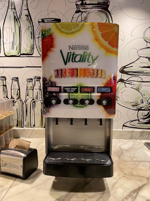 A Nestlé Vitality beverage dispenser on Royal Caribbean cruise ship with selections of strawberry, citrus passion, and peach flavors, alongside iced tea and water options.
