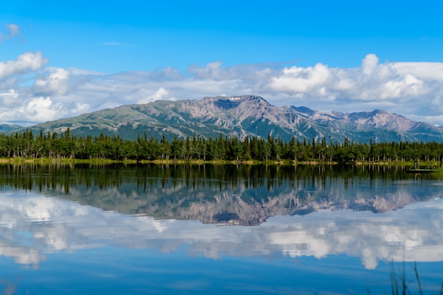 Scenic Alaska landscape with snow-capped mountains reflected in calm water and coniferous forest