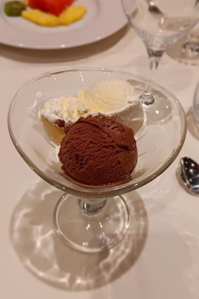 A dessert glass filled with scoops of vanilla and chocolate ice cream, a classic treat to enjoy after a meal. The image captures the creamy textures of the frozen dessert, ideal for those who appreciate the simple pleasures of traditional ice cream flavors.