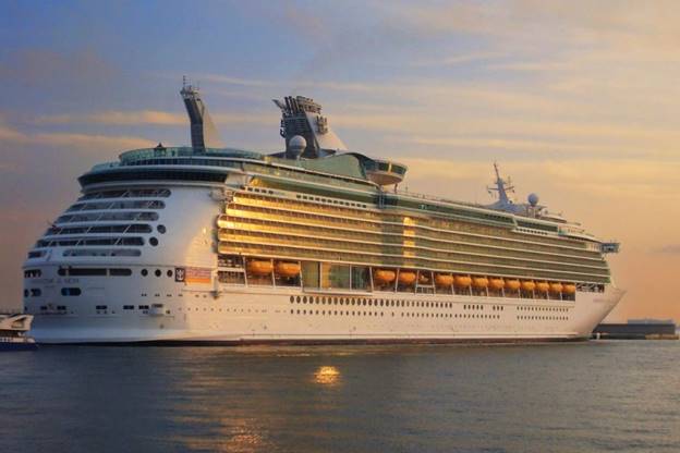 A majestic cruise ship, the Navigator of the Seas, basks in the warm glow of sunset as it docks at a port, its multiple decks illuminated, reflecting the fading sunlight.