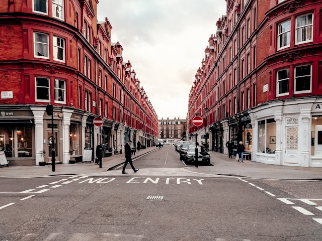 Quiet London street lined with red brick buildings, shops, and parked cars under an overcast sky.