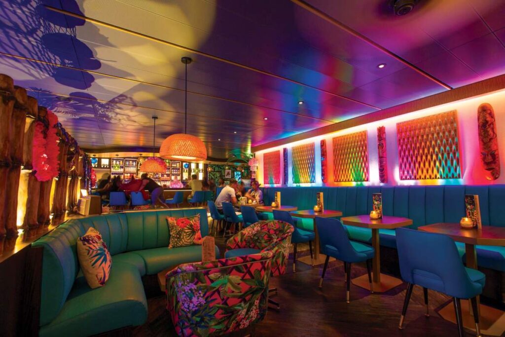 The Bamboo Room on Royal Caribbean's Mariner of the Seas, showcasing a vibrant tiki bar ambiance with colorful lighting, eclectic tropical-patterned furniture, and a warm, inviting atmosphere for guests enjoying drinks and conversation.