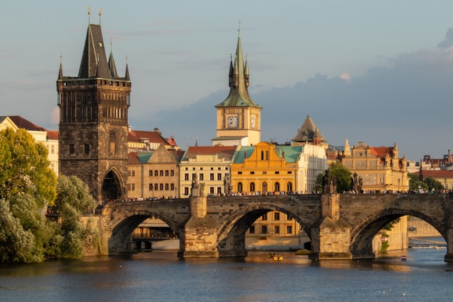 Charles Bridge spanning the Vltava River in Prague at golden hour, with historic towers and colorful Old Town buildings in the background.