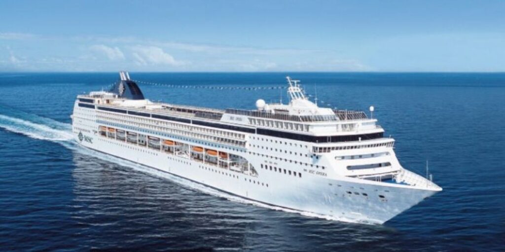 The MSC Opera cruise ship is captured cruising the open sea, featuring its distinctive navy blue and white exterior, multiple decks with lifeboats, and a sleek design, set against a backdrop of clear skies and calm waters.