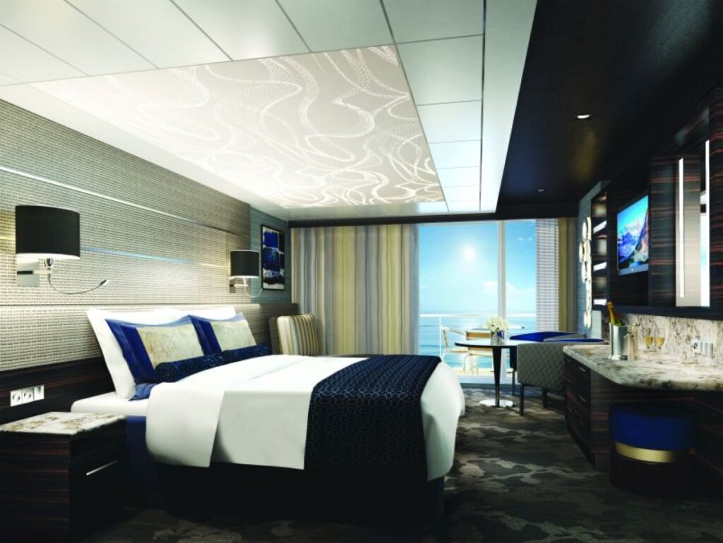 The Haven suite on the Norwegian Cruise Line Bliss features a luxurious and spacious design with a large bed, elegant decor, and a private balcony offering stunning ocean views. The suite includes modern amenities such as a flat-screen TV, a sitting area with a table and chairs, and a marble countertop with a vanity and storage. Soft lighting and sophisticated furnishings create a refined and comfortable atmosphere for guests.