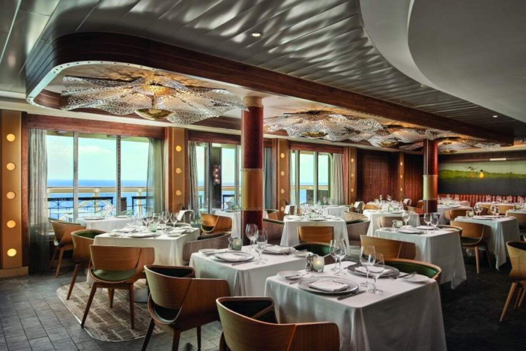 Elegant dining area inside Ocean Blue on Norwegian Bliss with neatly arranged tables, contemporary chairs, and large windows offering ocean views, showcasing a sophisticated onboard dining experience.