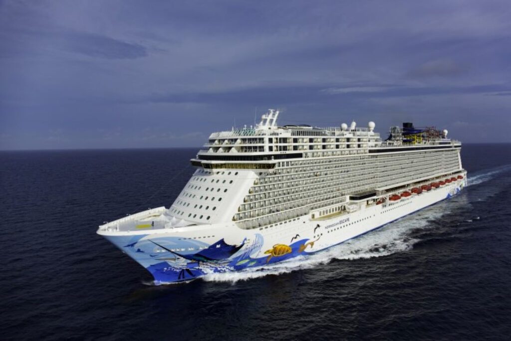 This image showcases the Norwegian Escape cruise ship sailing through open, deep-blue ocean waters under a cloudy sky. The ship's hull features vibrant marine-themed artwork, adding a touch of playfulness to its sleek, modern design. Its size and elegance emphasize a luxurious cruising experience in a serene maritime setting.