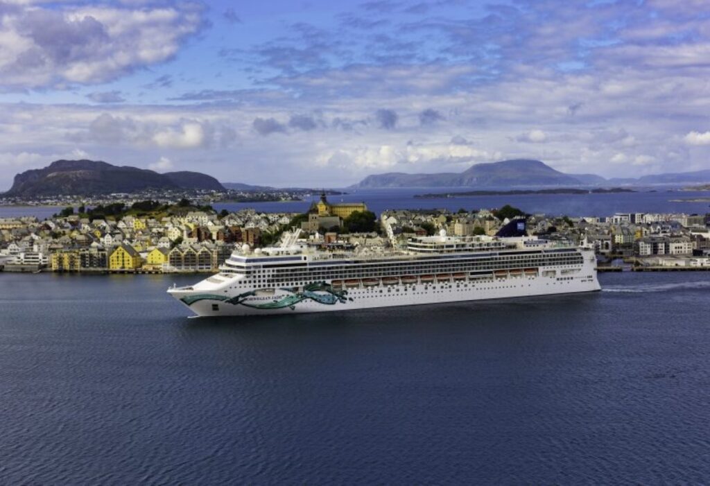 The Norwegian Jade cruise ship docked in the picturesque port of Ålesund, Norway, with its distinctive colorful buildings and majestic mountain backdrop, highlighting the ship's global itineraries.