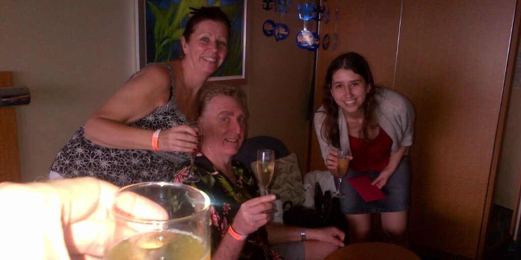 A cheerful family moment captured indoors with two women and a man raising their glasses for a toast, likely celebrating an occasion aboard a Royal Caribbean cruise. The room is adorned with festive decorations and the group exudes a sense of joy and togetherness.