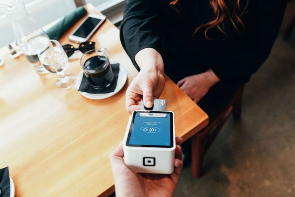 A person completes a contactless payment using a smartphone over a portable card reader, representing the modern and convenient method of settling gratuities on a Royal Caribbean cruise.