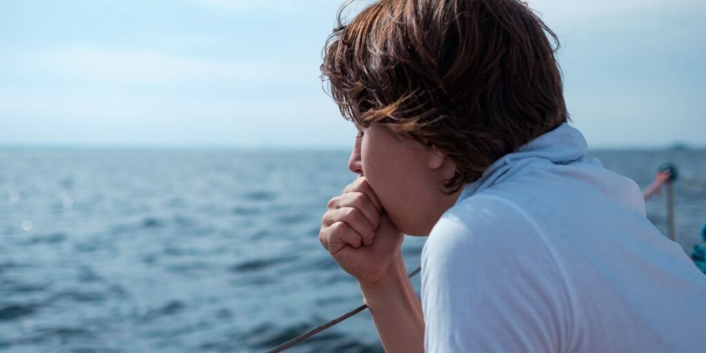 A teenager holding back a vomit on the side of a cruise