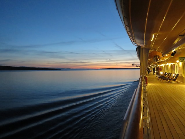Empty cruise ship promenade deck at dusk with warm golden lighting and twilight sky reflected in calm ocean