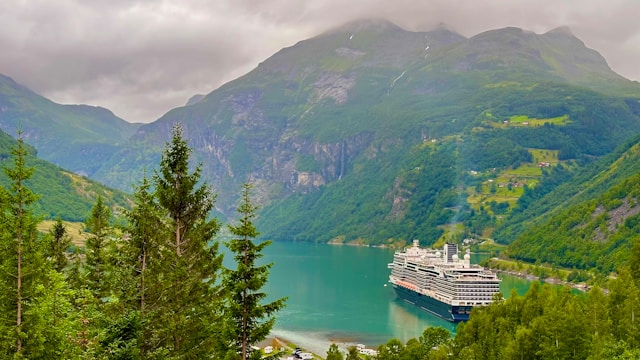 Cruise ship sailing through a narrow fjord surrounded by steep green mountains and calm water.