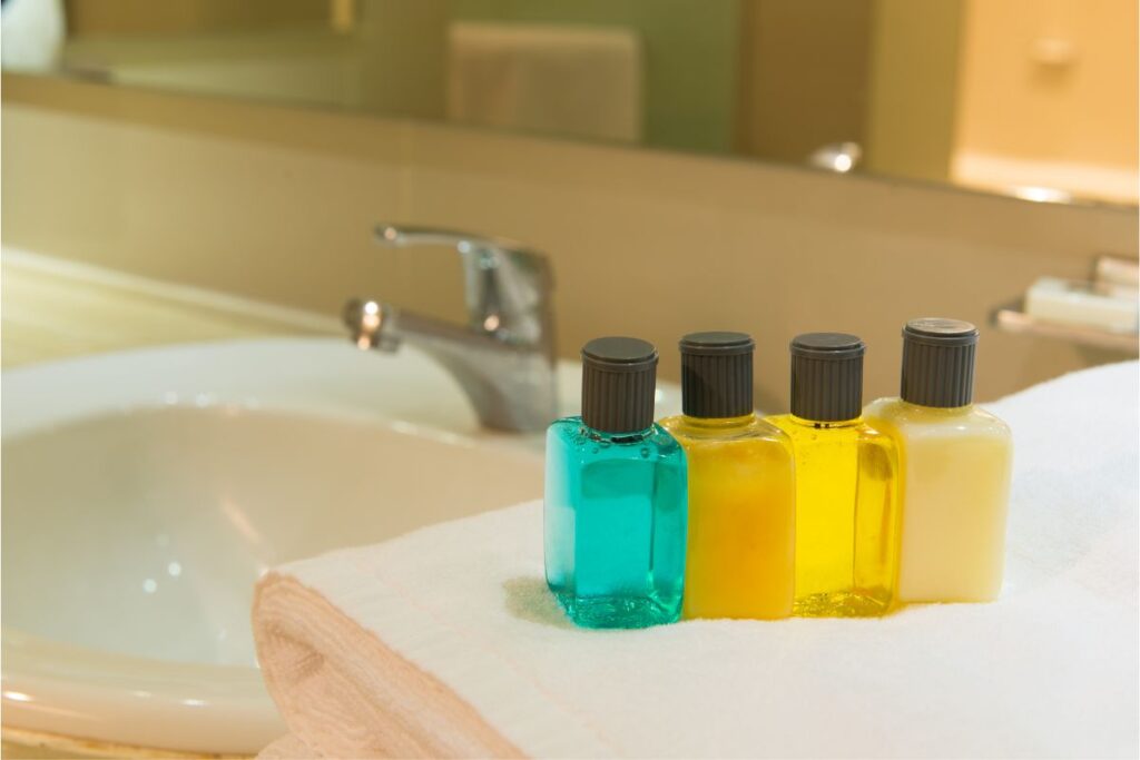 The image shows small bottles of toiletries, including shampoo, conditioner, and lotion, placed on a neatly folded white towel. The setup is located near a bathroom sink with a silver faucet, reflecting the clean and organized look of a cruise ship bathroom.