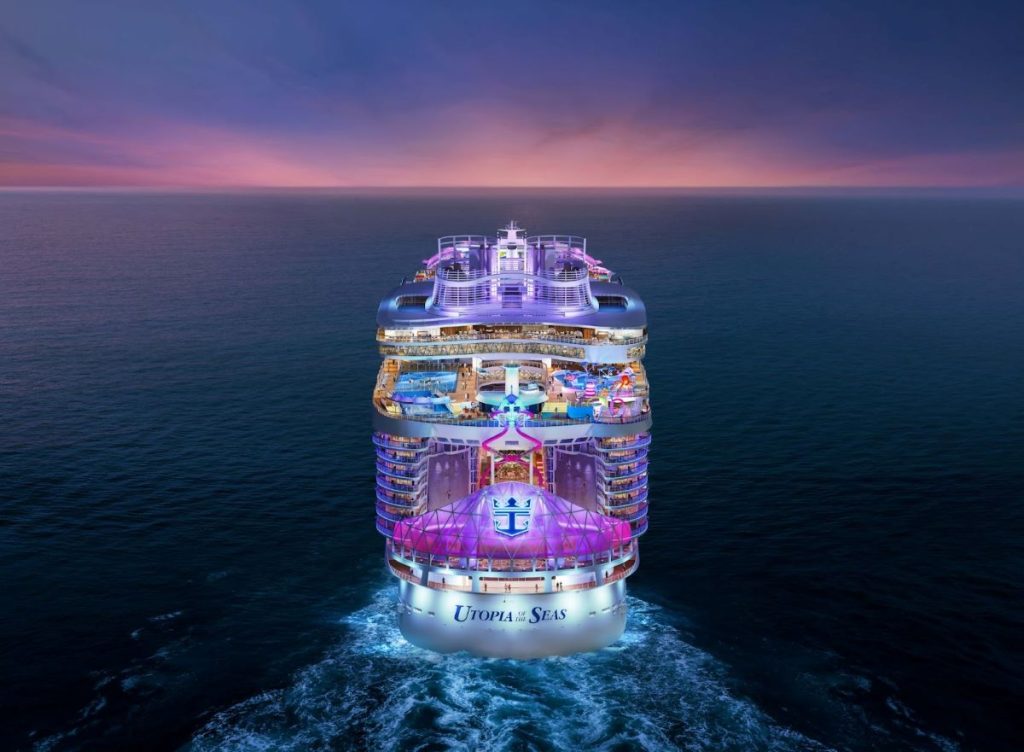 Royal Caribbean's Utopia of the Seas cruise ship sailing at dusk, with vibrant lighting accentuating its multiple decks and leisure amenities against a backdrop of a purple-tinged sky and calm sea.
