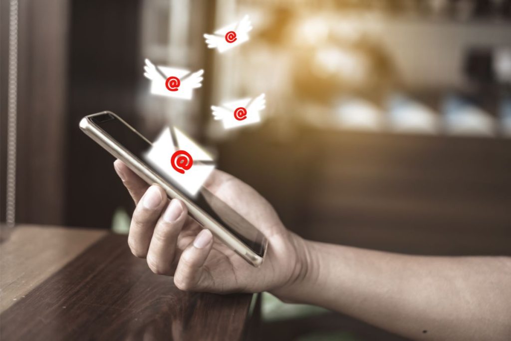 Close-up of a person's hand holding a smartphone with illustrated email icons and envelopes with wings fluttering around the screen, symbolizing incoming messages.