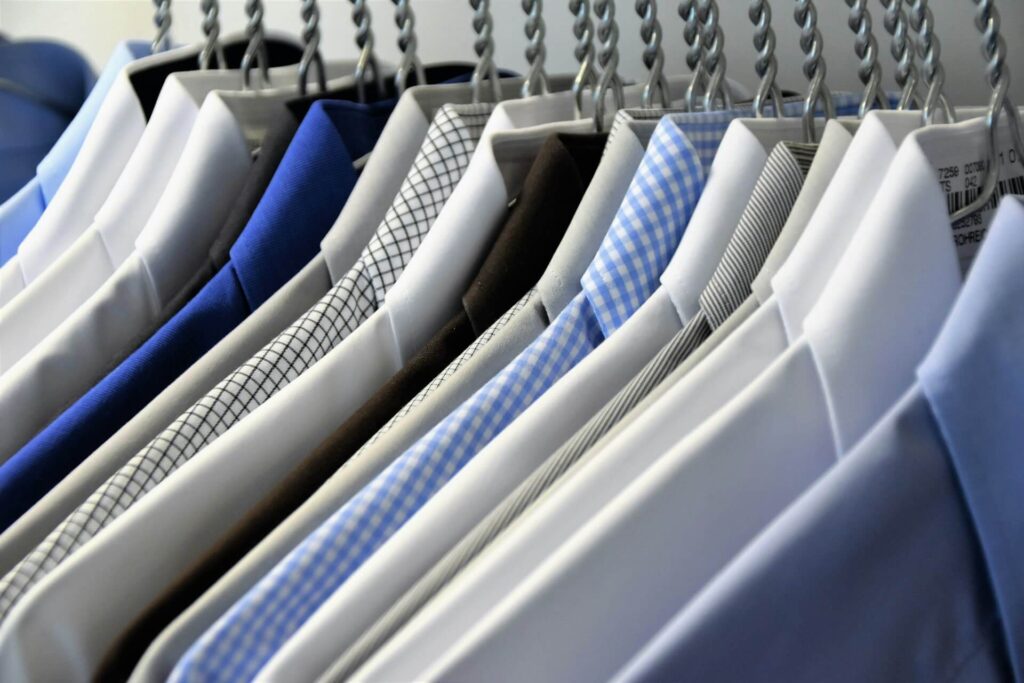 Row of dress shirts and neckties hanging on a clothing rack, in white, blue, and patterned fabrics.
