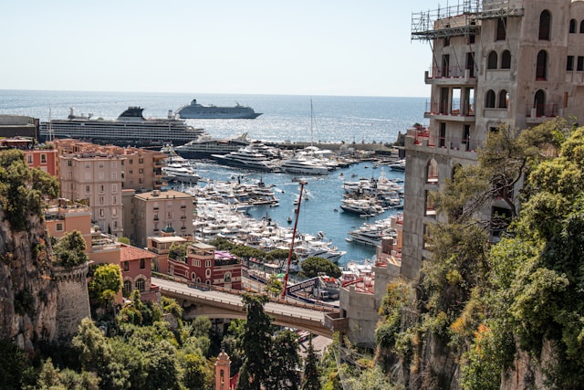Cruise ships off the coast of a Mediterranean port in Monaco, overlooking a marina packed with yachts and hillside buildings.